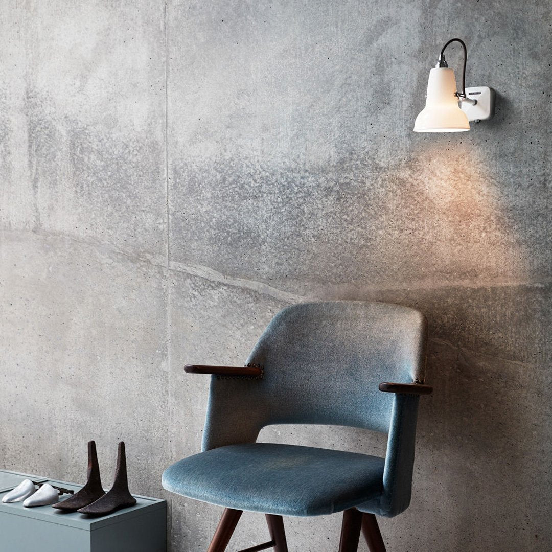 Light gray wall, blue chair with wooden legs, white lamp, black and white footwear on concrete floor.