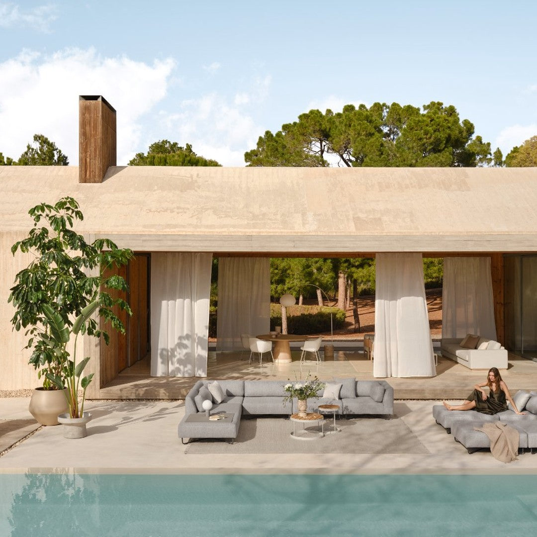 Modern outdoor lounge with gray sofas and decor, set against a natural backdrop and serene blue pool.