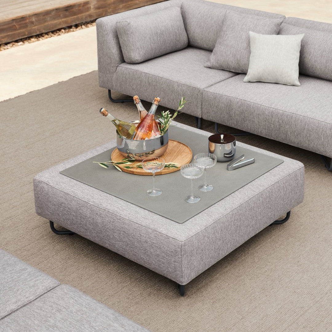 Gray upholstered coffee table with a sleek glass top, paired with soft textures and natural tones.