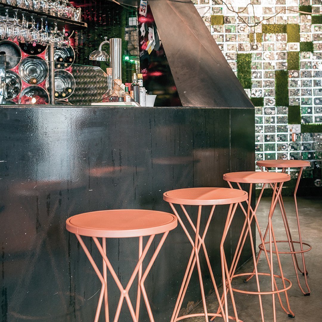 Rose gold bar stools with geometric wire design against a black and white patterned wall. Modern and stylish decor.