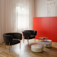 Black velvet armchairs with silver legs, surrounded by white and gray tables against a bright red wall.