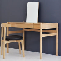 "Light oak desk with a minimalist design, paired with a black cushioned chair against a dark gray wall."