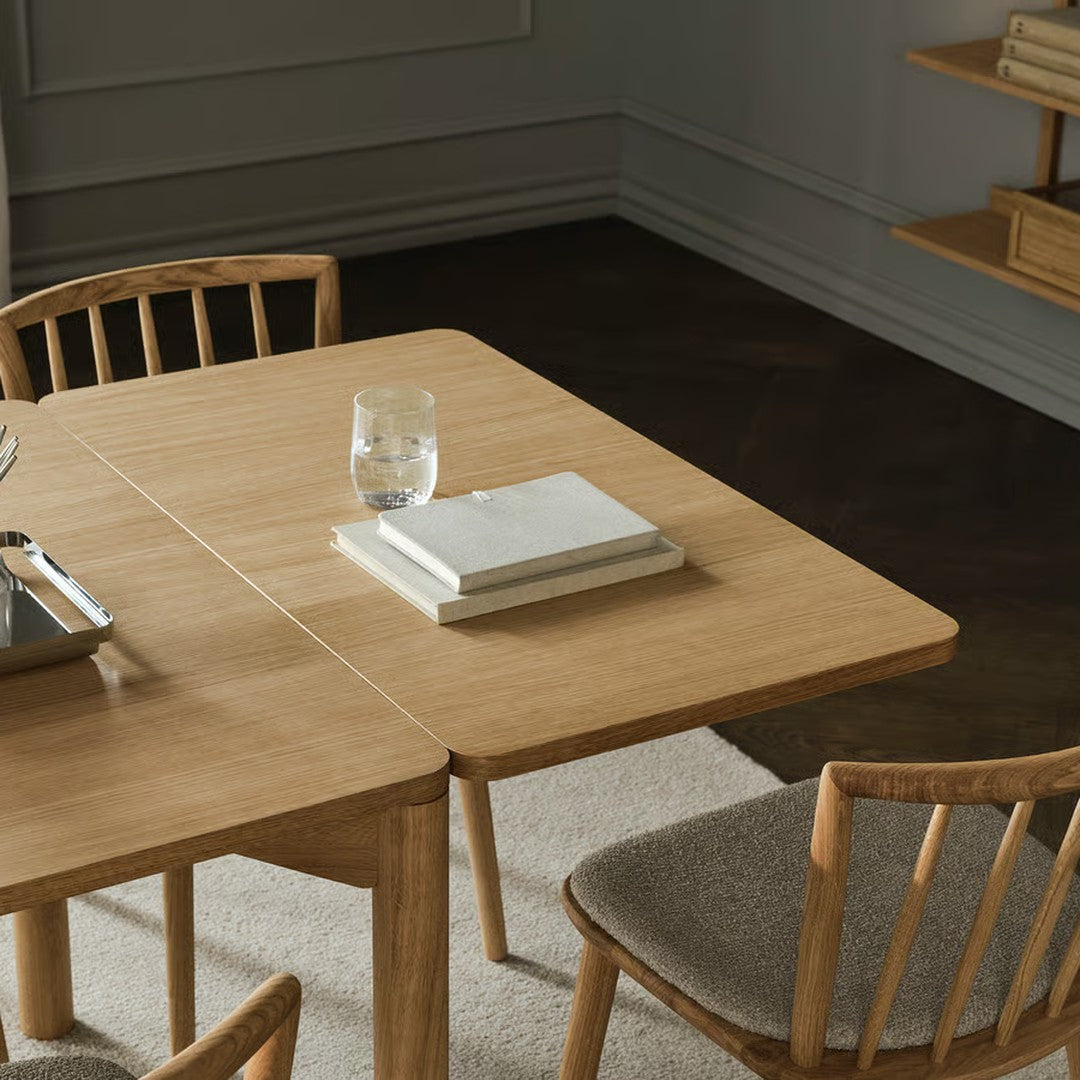 Light oak wood table with a natural finish, paired with neutral beige chairs and a soft gray rug. Simple, elegant design.