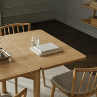 Light oak wood table with a natural finish, paired with neutral beige chairs and a soft gray rug. Simple, elegant design.