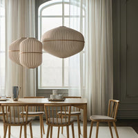 Beige striped pendant lights hanging above a wooden dining table with light-colored chairs and sheer white curtains.