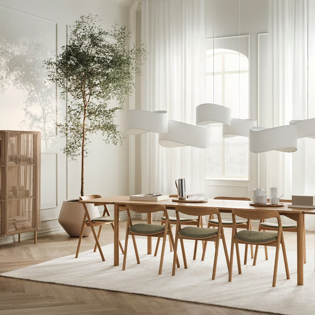 Light wood dining table with green accents, soft white curtains, and neutral tones create a modern, airy dining space.