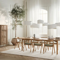Modern dining room featuring light wood furniture, soft green cushions, and white accents surrounded by natural light.