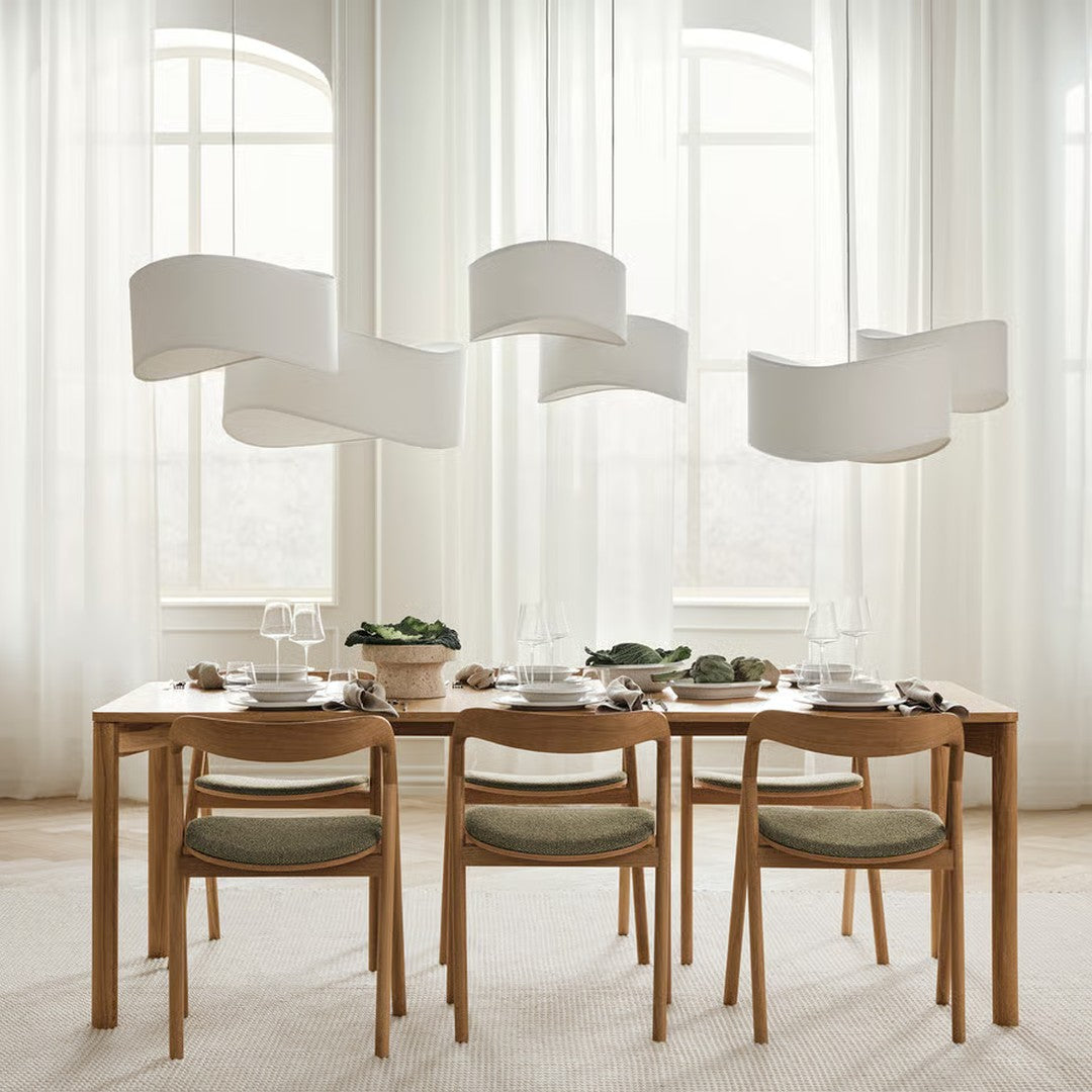 "Light wooden dining table with green cushions, white decor, and soft, flowing curtains in a bright, airy space."