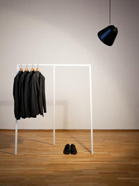 Black suits on a white hanger, black shoes on a wooden floor, and a black pendant light above. Simple, modern aesthetic.