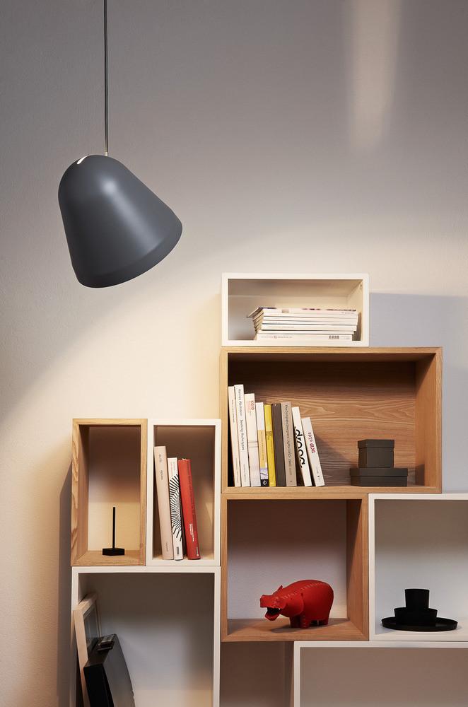 Gray pendant light hangs over a light wood bookshelf with white and dark accents, featuring colorful decor.