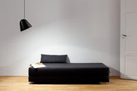 Black minimalist daybed with a simple texture, set against a light gray wall and warm wooden floor.
