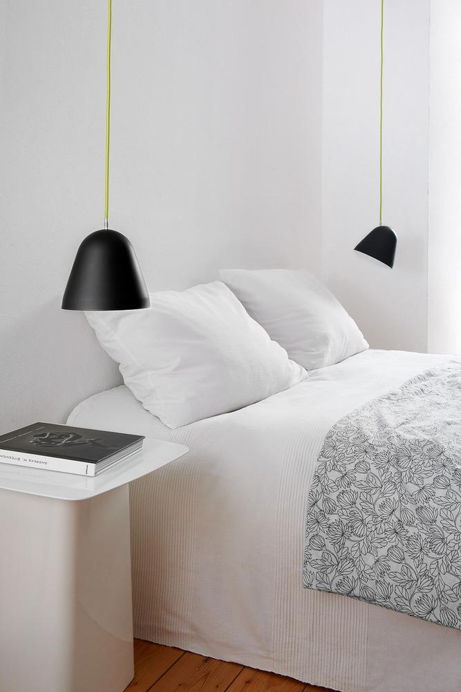 Black pendant lights hang over a white bed with textured gray bedding and a minimalist nightstand.