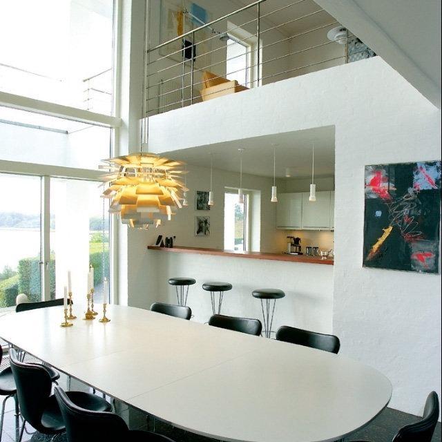 Modern dining area with a sleek white oval table, black chairs, and vibrant pendant light against a light-toned backdrop.
