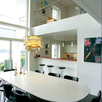 Modern dining area with a sleek white oval table, black chairs, and vibrant pendant light against a light-toned backdrop.