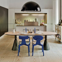 Oval light wood dining table with black and blue accent chairs, set against a modern kitchen backdrop.