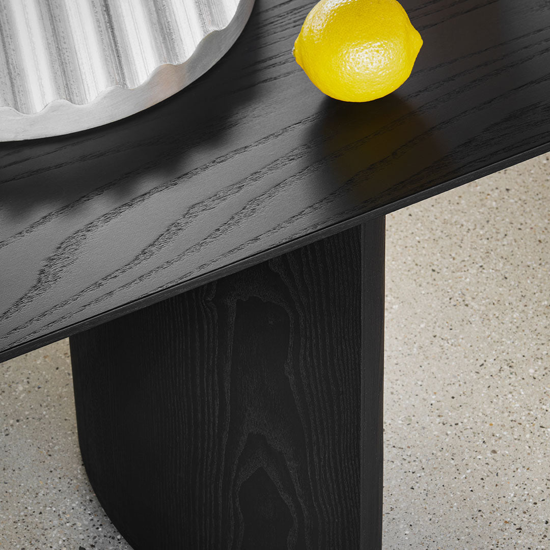 Black wooden table featuring a smooth finish, paired with a silver dish and a vibrant yellow lemon on a light speckled surface.