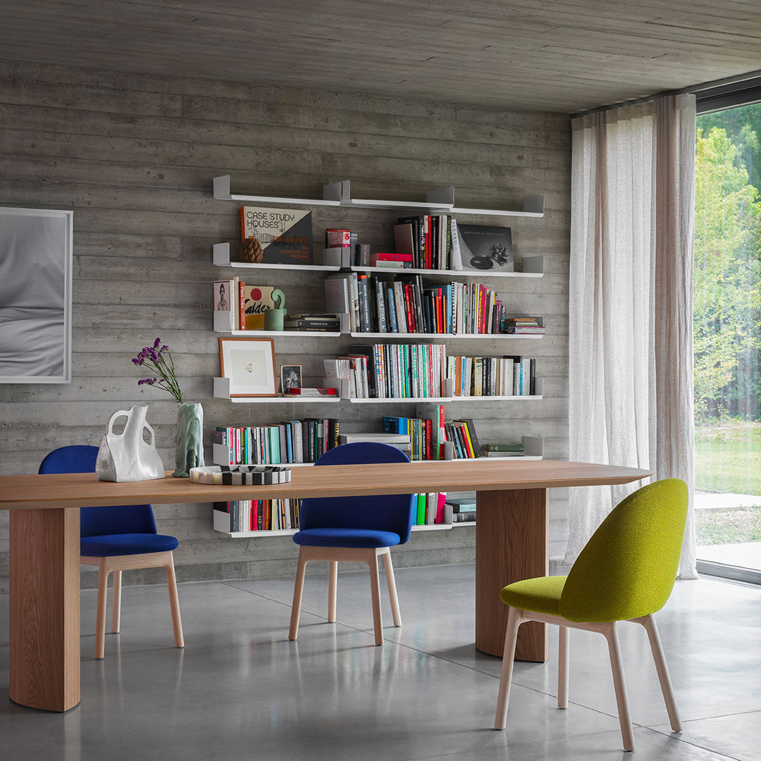 Modern dining room with a wooden table, blue chairs, and a vibrant green chair against a neutral concrete backdrop.