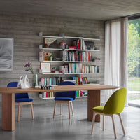 Modern dining room with a wooden table, blue chairs, and a vibrant green chair against a neutral concrete backdrop.