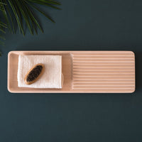 Light wooden rectangular tray with ridges, featuring a white towel and black caviar, set against a dark green surface.