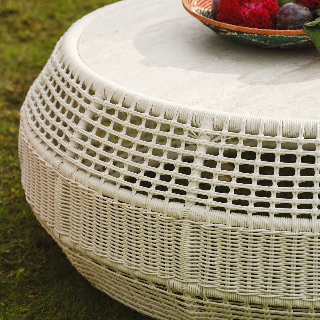 Round woven coffee table in white with a textured pattern, featuring a smooth, light stone top and a natural grass background.