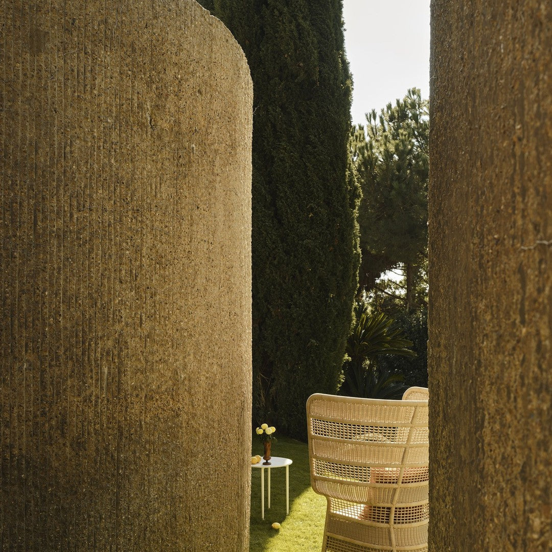 Natural tones and textures of earthy brown columns, lush green grass, and a light beige chair in a serene outdoor setting.