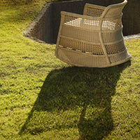Beige woven chair casting a shadow on green grass, showcasing a textured pattern and natural design.