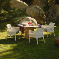 White outdoor chairs surround a round table with a vibrant purple tablecloth, set on lush green grass.