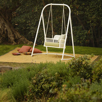 White swing chair with a sleek design, surrounded by green grass and earth-toned cushions on a golden mat.