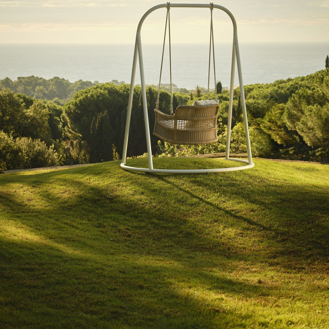 Light beige swing with a minimalist white frame, set against lush green grass and a serene natural backdrop.