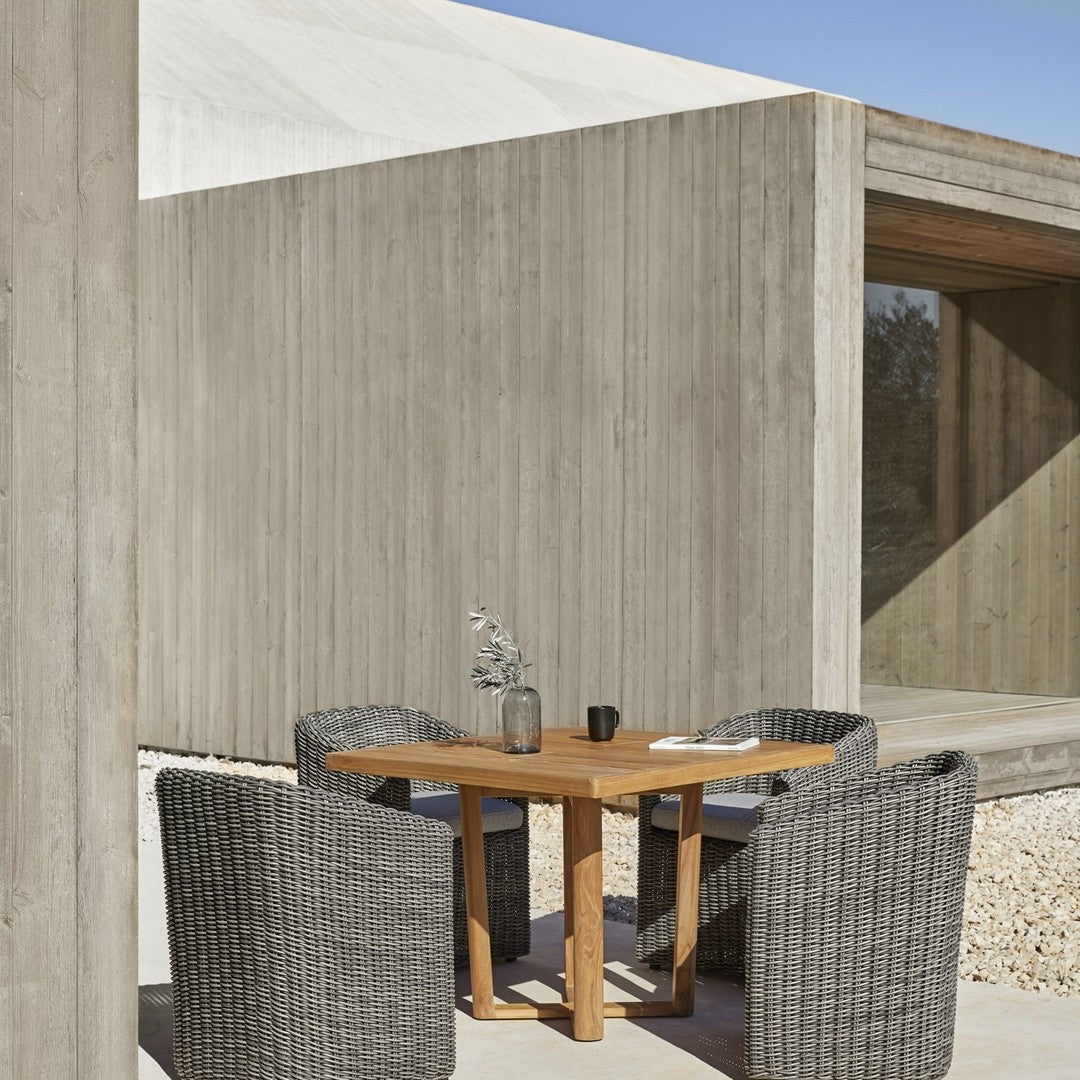 Modern outdoor dining set featuring grey woven chairs and a natural wood table against a minimalist concrete backdrop.