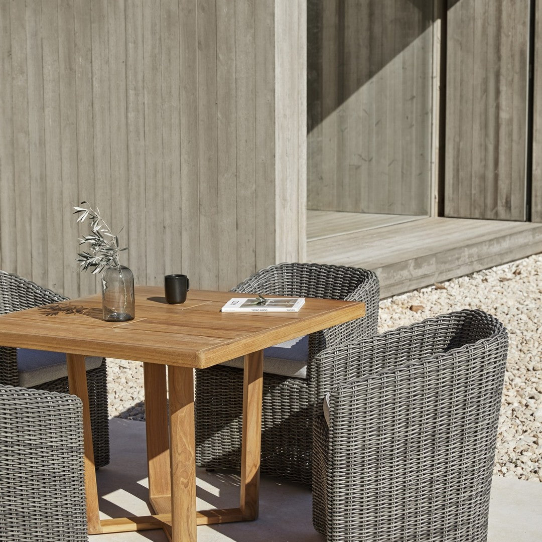 Gray woven chairs surround a wooden table, set against a minimalist concrete backdrop.