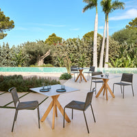Outdoor dining set featuring gray chairs and a light wood table, set against a serene green landscape and blue pool.