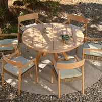 Natural wood round dining table with beige cushions and light-toned chairs, set on a textured neutral rug.