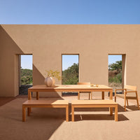 Light wood dining set with a minimalist design, set against earthy-toned walls and a clear blue sky.