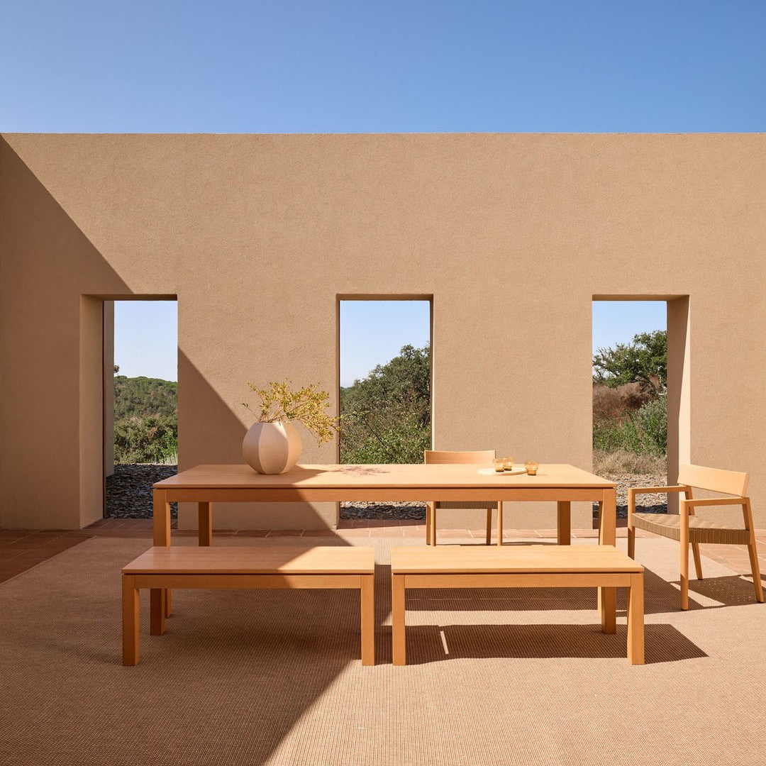 Light wood dining table and benches against a warm, neutral-toned wall with natural light and minimalistic design.