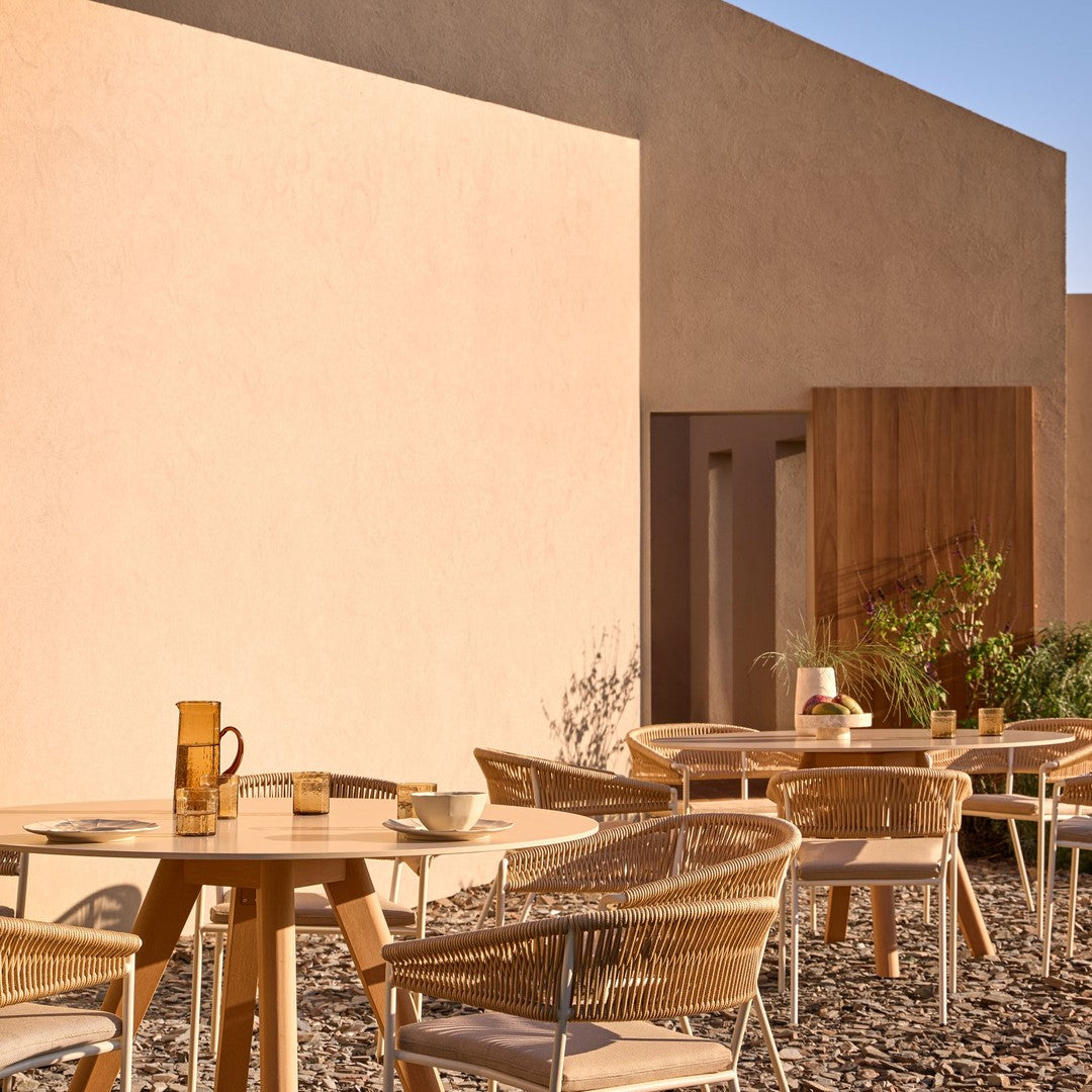 "Elegant outdoor dining set with beige and natural tones, featuring woven chairs and wooden tables against a textured wall."