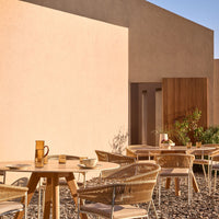 "Elegant outdoor dining set with beige and natural tones, featuring woven chairs and wooden tables against a textured wall."