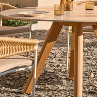 Round beige table with natural wood legs; woven tan chairs complementing a textured stone surface.