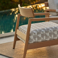 Light wood chair with a geometric gray and cream patterned cushion, set against a serene outdoor backdrop.