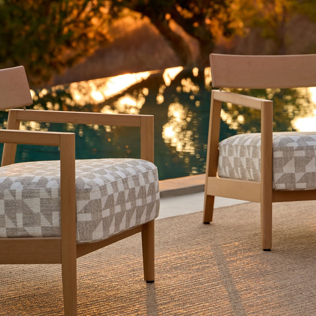 Natural wood chairs with textured beige and gray geometric patterned cushions, set against a serene outdoor backdrop.