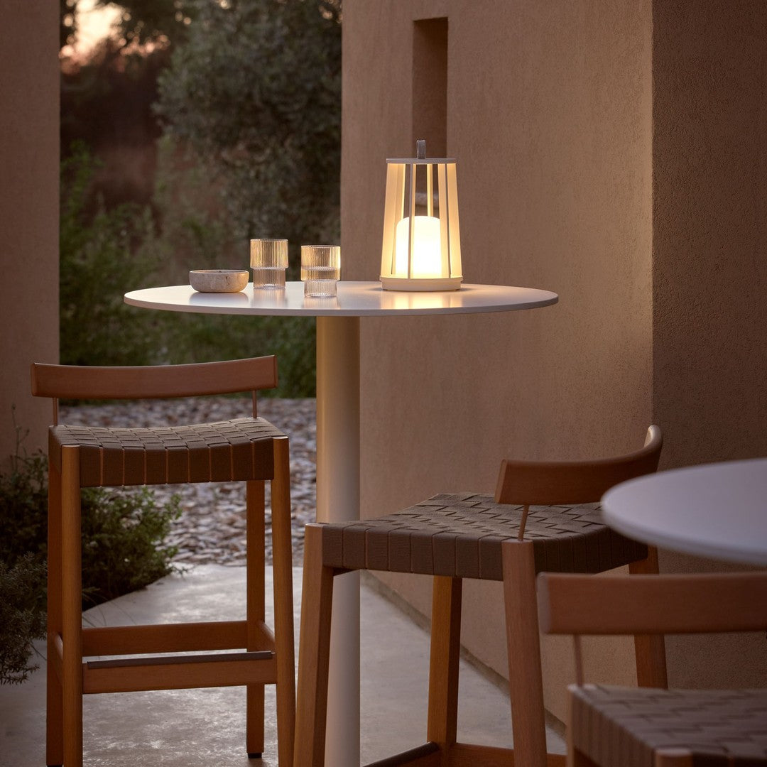 Modern outdoor table with a sleek white top, natural wood chairs, and soft glowing lantern, perfect for evening ambiance.