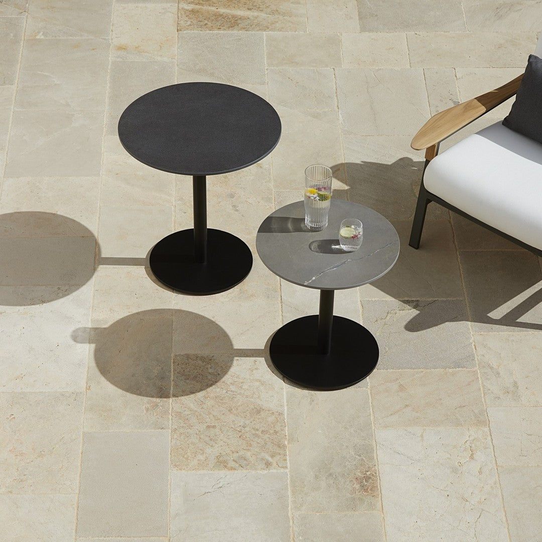 Black and gray round side tables with sleek finishes, set on light stone flooring.