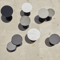 Modern circular tables in black, white, gray, and marble patterns, casting unique shadows on a light stone surface.