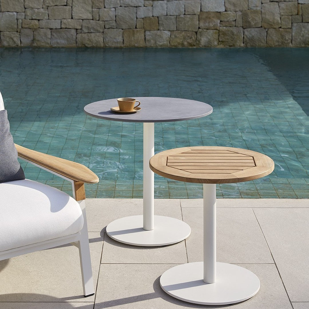 "Modern round tables with grey and wood finishes, featuring white metal bases, near a serene pool backdrop."