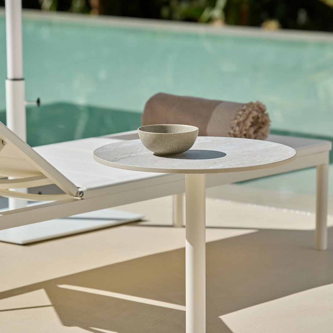 Stylish white table with a round top, beige towel, and minimalist bowl set against a serene pool backdrop.