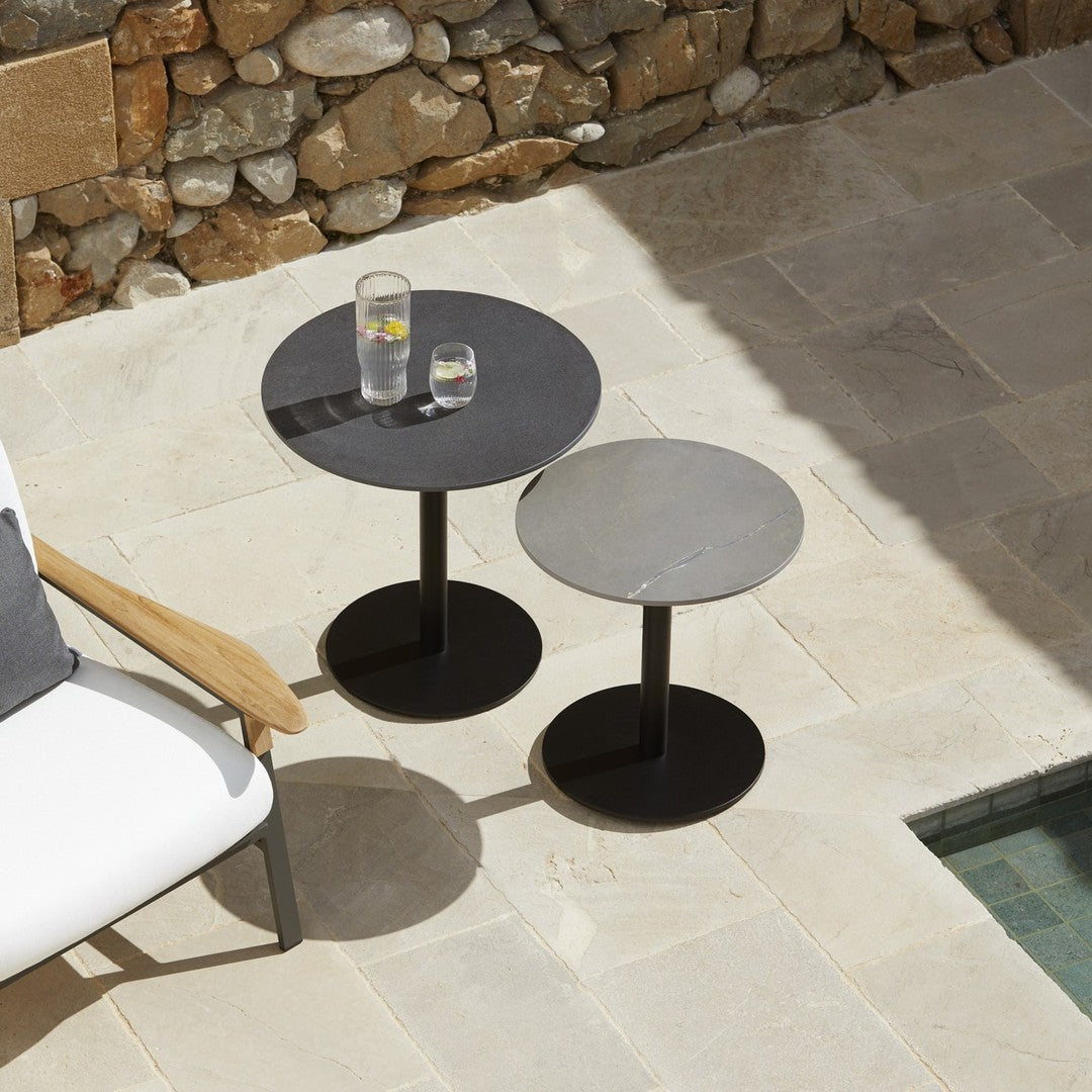 Two modern side tables in black and gray, featuring smooth circular tops and sleek bases, set on a stone patio.