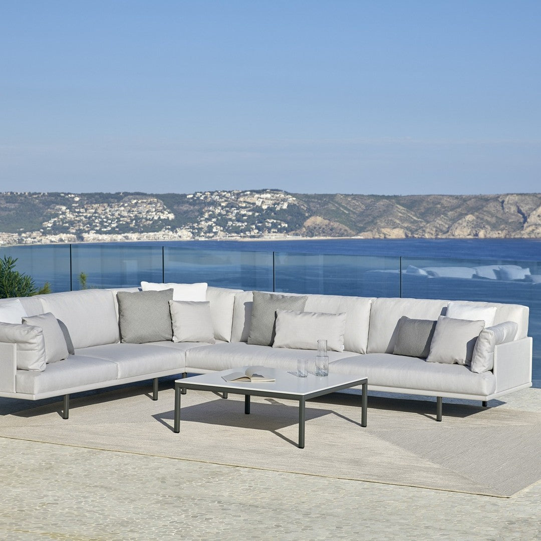 Modern gray outdoor sectional sofa with soft cushions, paired with a sleek black metal coffee table and a neutral rug.
