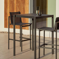 Modern black bar table and chairs with sleek lines, set against a wood-paneled background.