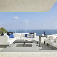 Coastal-inspired outdoor sectional sofa with white cushions, blue and white patterned throw pillows, and grey rug.