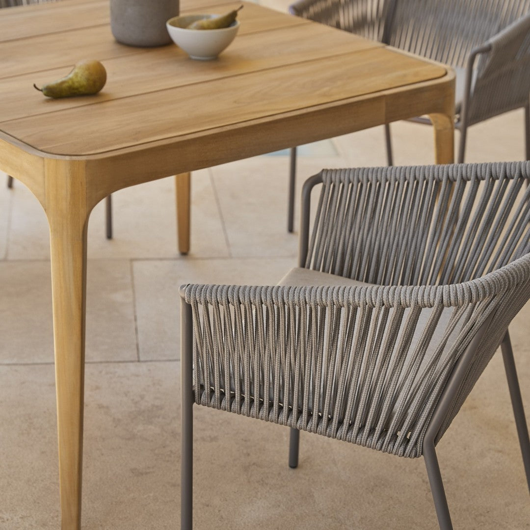 Natural wood dining table with a light finish and a grey woven chair, perfect for modern outdoor settings.